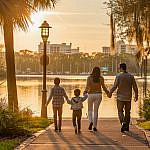 A family strolls along the Lake Mirror Promenade in Lakeland, Florida, surrounded by calm water, gardens, and evening light—a perfect start to a family adventure.
