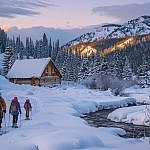 A family snowshoes toward a secluded cabin in the Vallecito Creek Basin of San Juan National Forest, capturing the quiet magic of Colorado winter cabins far from the ski resort crowds.