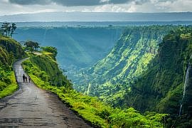 Wide landscape view of Bolaven Plateau Laos with forested hills, waterfalls, and a family walking along a rural road