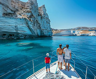 Family enjoying a Greece yacht charter near Kleftiko on Milos with dramatic sea cliffs and turquoise water.