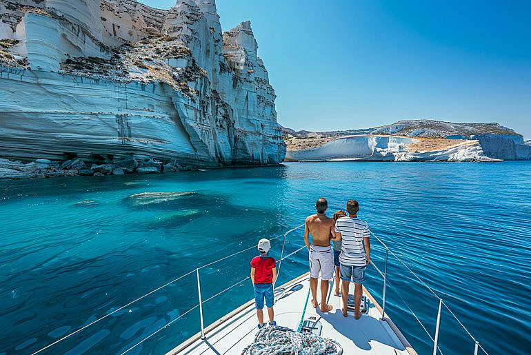 Family enjoying a Greece yacht charter near Kleftiko on Milos with dramatic sea cliffs and turquoise water.
