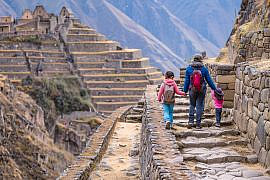 Family viewing Machu Picchu with kids from a trail overlooking the Inca citadel and Huayna Picchu in Peru.