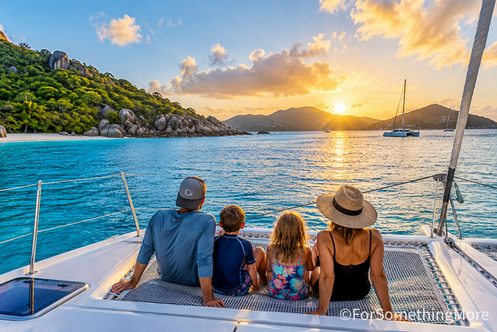 Family relaxing on the bow of a catamaran at sunset during a family sailing adventure.