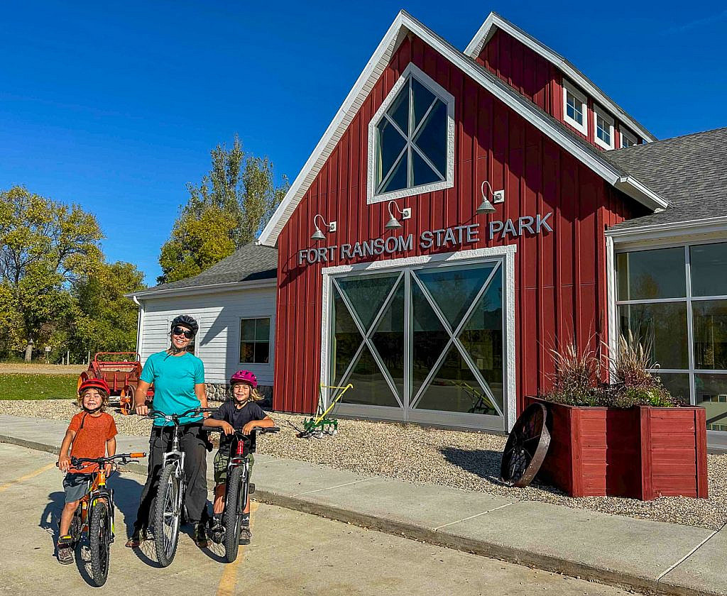 Family with two young boys and mountain bikes outside the Fort Ransom State Park Visitor Center in North Dakota’s Sheyenne River Valley during fall.
