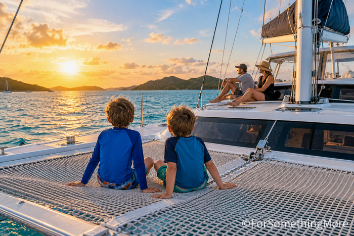 Children relaxing on the foredeck of a catamaran during an island-hopping family sailing trip.