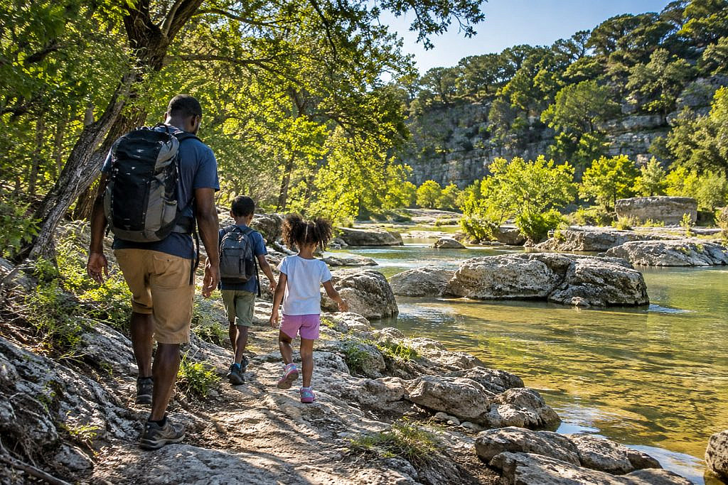 Alt text: Parent and two children hiking beside a creek during a Texas Hill Country with kids adventure near Austin.