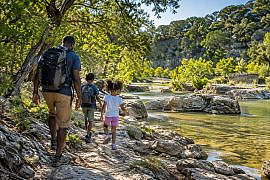 Alt text: Parent and two children hiking beside a creek during a Texas Hill Country with kids adventure near Austin.