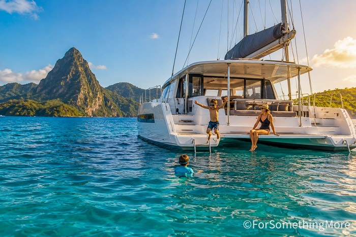 Family swimming beside a sailing catamaran during a tropical family sailing adventure.