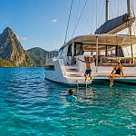 Family swimming beside a sailing catamaran during a tropical family sailing adventure.