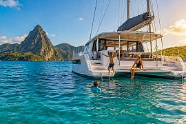 Family swimming beside a sailing catamaran during a tropical family sailing adventure.