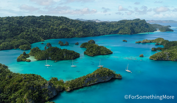 Sailing catamarans anchored among lush tropical islands and turquoise water during a family sailing adventure.